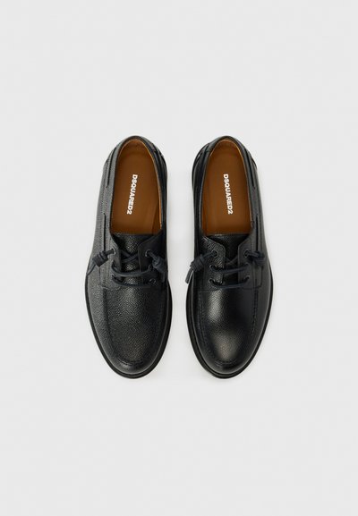Chaussures en cuir noir avec finition texturée, bout rond et design à lacets. Intérieur beige avec logo. Semelle plate noire.