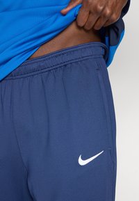 Tmavomodré športové šortky s elastickým pásom, s bielym logom Nike Swoosh na ľavej strane. Materiál pôsobí ľahko a hladko.