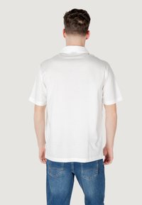 Polo shirt bianco a maniche corte con retro semplice, realizzato in un tessuto morbido e dotato di colletto standard, abbinato a jeans in denim blu.