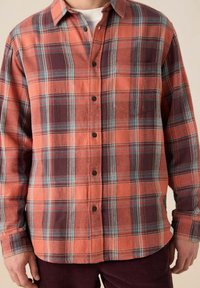 Geruite flanellen blouse met oranje, bordeaux en turquoise tinten; knoopsluiting aan de voorkant, lange mouwen en een borstzak. Gemaakt van zacht materiaal.
