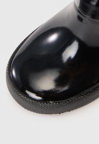 Botte de pluie noire et brillante avec un bout arrondi, semelle en caoutchouc noir texturé et détails de couture autour de la base. Fini lisse avec un haut éclat.