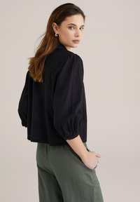 Top corto nero con maniche a sbuffo, realizzato in un tessuto morbido. Abbinato a pantaloni verdi larghi, con una vestibilità rilassata e tasche laterali.