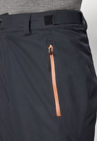 Black outdoor pants with textured fabric, featuring a prominent bright orange zippered pocket and adjustable waistband.