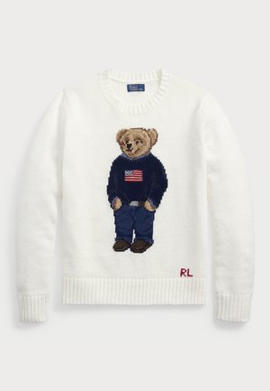 Weißer Strickpullover mit geripptem Saum, ausgestattet mit einem gestickten Bären in einem dunkelblauen Pullover mit einer US-Flagge und dunklen Jeans, signiert "RL".