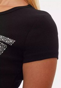 Musta lühikeste varrukatega T-särk, mille esipinnal on sädelev rhinestone graafika. T-särgil on sile kangastruktuur ja kitsas lõige.