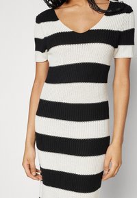 Schwarz-weißer gestreifter Strickkleid mit V-Ausschnitt und kurzen Ärmeln; hat eine taillierte Form und eine gerippte Textur.