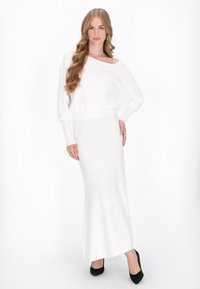 Suéter blanco de manga larga y fuera de los hombros combinado con una falda maxi blanca ajustada. Unos zapatos de tacón negro completan el look.