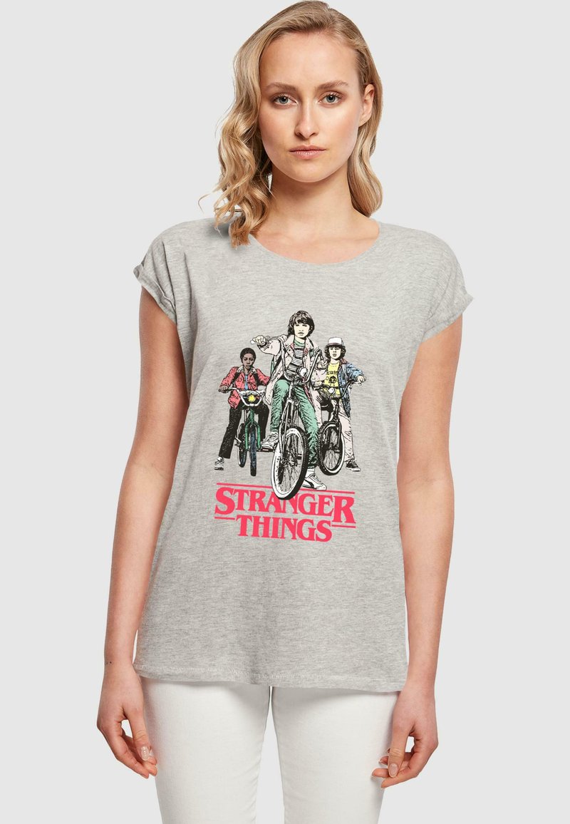 Szara bawełniana koszulka z grafiką trzech postaci na rowerach, z wyraźnym czerwonym napisem "STRANGER THINGS" pod wzorem.