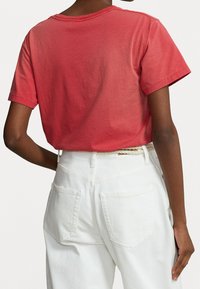 Röd bomullströja med korta ärmar, rund halsringning och en något avslappnad passform, kombinerad med vita högmidjade jeans som har bakfickor.