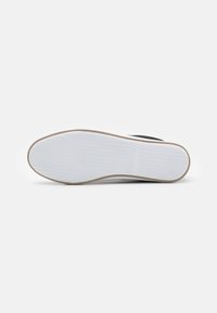 Suela de goma blanca con una superficie texturada, que presenta una parte superior negra. El diseño incluye un sutil tacón curvado y un acabado suave.
