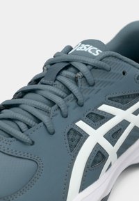 Gray athletic shoe with a textured upper, white accents, and intricate mesh detailing, featuring flat laces and a cushioned sole.