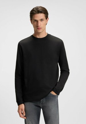 Schwarzes Langarm-T-Shirt aus weichem Stoff mit rundem Halsausschnitt und gerippten Bündchen, kombiniert mit hellgrauen Jeans. Keine Muster oder Verzierungen.