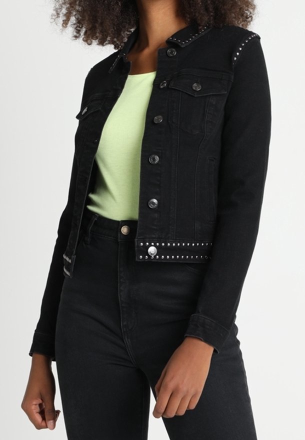 Chaqueta de denim negra con tachuelas plateadas, dos bolsillos en el pecho y botones a presión, combinada con una blusa verde clara y jeans negros de tiro alto.