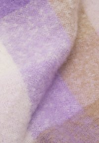 Tissu doux et plié avec une texture duveteuse présentant un motif de couleurs pastel composé de carrés lavande, beige et blanc cassé.