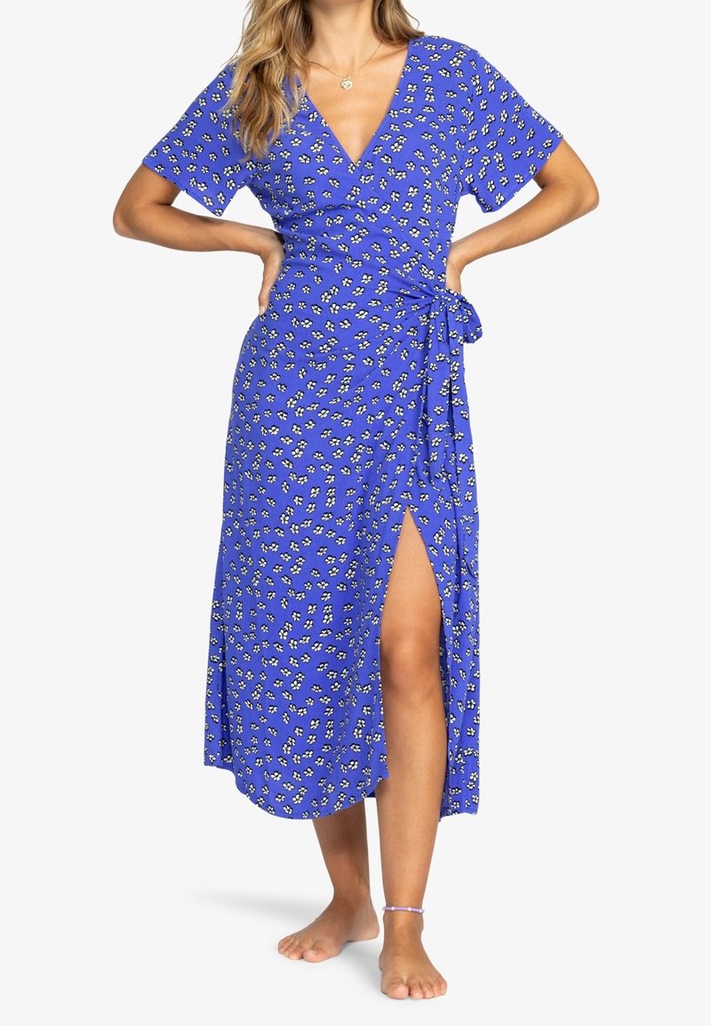 Robe maxi en tissu bleu vif avec motif floral blanc, décolleté en V, manches courtes, design enveloppant avec fente latérale et lien à la taille.