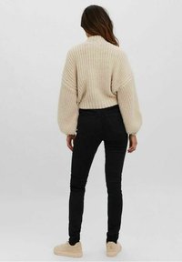 Gruby sweter z dzianiny w kremowym kolorze z szerokimi rękawami; zestawiony z dopasowanymi czarnymi dżinsami i jasnobeżowymi butami. Prosty i swobodny design.
