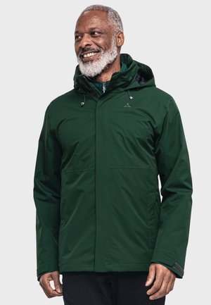 La chaqueta impermeable de color verde oscuro cuenta con un capucha, cuerdas ajustables y dos bolsillos frontales. La tela es suave y tiene un ligero brillo.