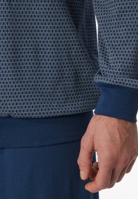 Tengerészkék, hosszú ujjú ing krémszínű, geometrikus méhsejt mintával. Bordázott mandzsetták, sima textúra és egyszínű sötétkék szegély.