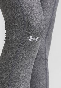 Leggings atletici grigi con una finitura strutturata, dotati di cuciture a contrasto e di un logo bianco sulla coscia. Il design aderente migliora la mobilità.