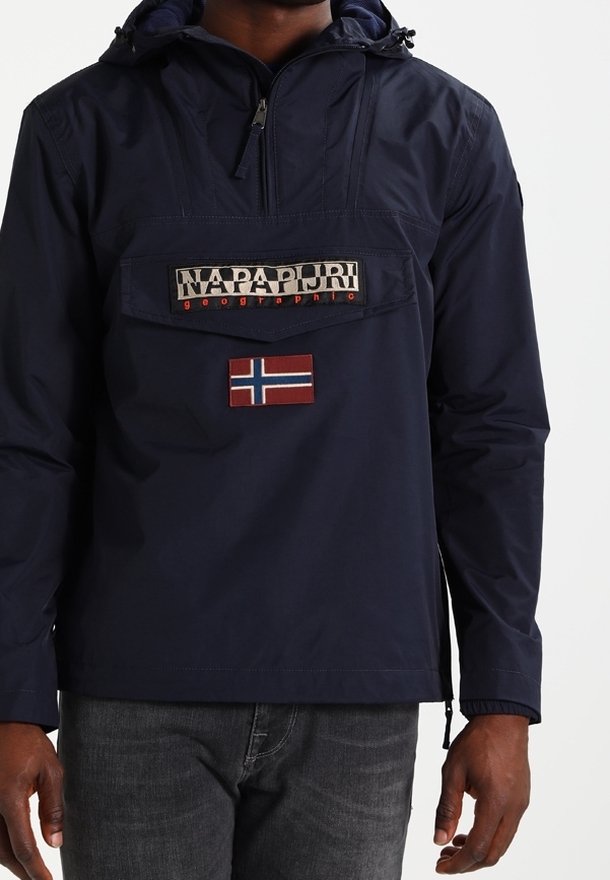 Marineblå pullover jakke med en frontlomme, der har et "Napapijri" logo og et Norge flag patch, lavet af vandtæt materiale med hætte.