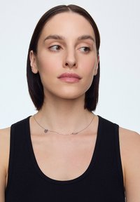 Srebrny naszyjnik z dwoma zawieszkami w kształcie serca, na modelce w czarnej koszulce na ramiączkach. Gładka, cienka łańcuszek podkreśla design.