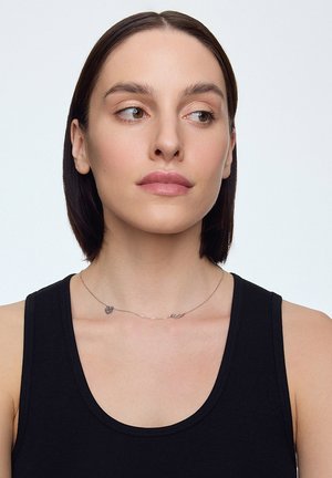 Srebrny naszyjnik z dwoma zawieszkami w kształcie serca, na modelce w czarnej koszulce na ramiączkach. Gładka, cienka łańcuszek podkreśla design.