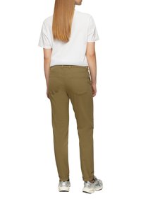 Olivgrüne Hose im Slim Fit mit Five-Pocket-Design und Gürtelschlaufen, kombiniert mit einem schlichten weißen T-Shirt und silbernen Sportschuhen.