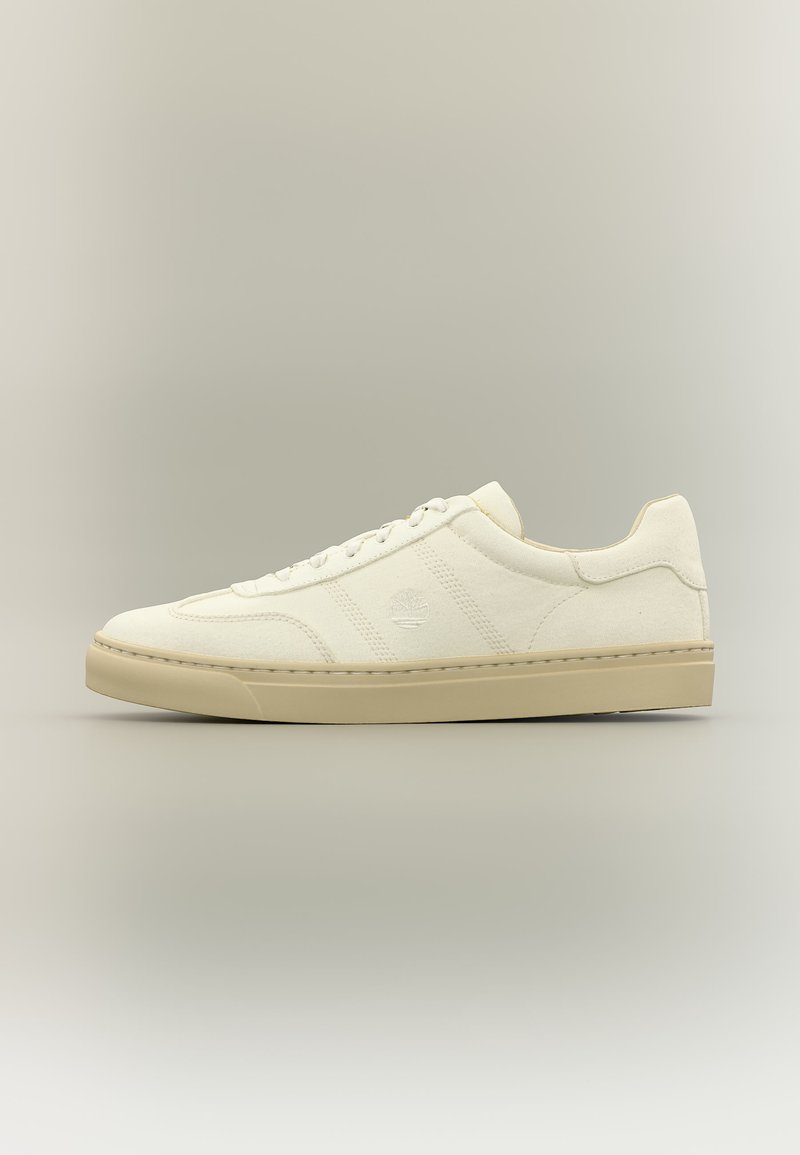 Pantof sport off-white cu talpă bej, design cu șireturi și logo subtil embosat pe lateral, prezentat pe fundal neutru.