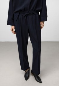 Hosen mit maritimen Muster, verstellbarem Bund, strukturiertem Stoff und geradem Schnitt, kombiniert mit schlichten schwarzen Pumps.