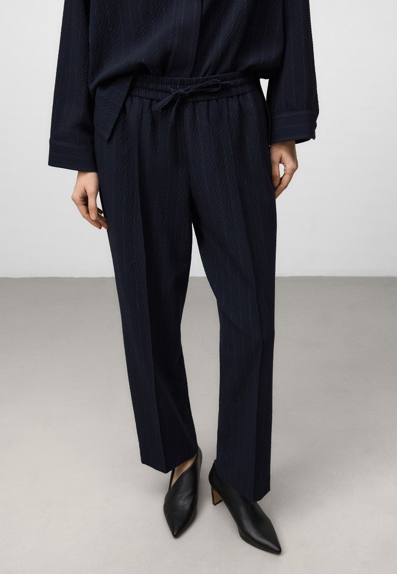 Hosen mit maritimen Muster, verstellbarem Bund, strukturiertem Stoff und geradem Schnitt, kombiniert mit schlichten schwarzen Pumps.