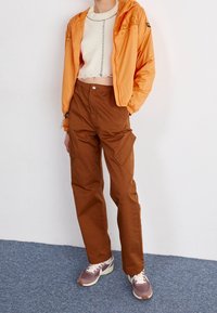 Pomarańczowa krótka kurtka z zapięciem na zamek; biała sweterkowa bluzka; brązowe spodnie cargo z bocznymi kieszeniami; szaro-białe sneakersy.