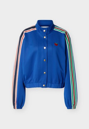 Modrá bunda na zips s viacfarebnými pruhmi na rukávoch, zlatými patentkami na prednej strane, elastickým lemom a malou červenou výšivkou jahody na hrudi.