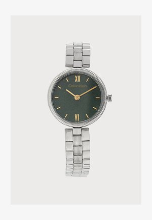Montre bracelet en métal argenté avec cadran noir, marqueurs d'heure dorés et logo Calvin Klein, affichant l'heure 10:10.