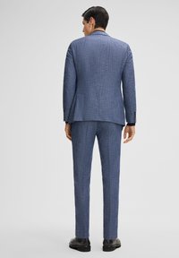 Completo a scacchi blu con design su misura; tessuto leggero; pantaloni dritti; texture sottile; scarpe nere visibili in basso.