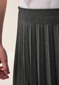 Plissé zwarte denimrok met een gestructureerde afwerking en een getailleerde tailleband. Hand rustend op de stof toont de plooien en ontwerpdetaillering.