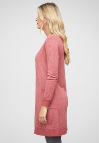Cardigan en tricot rouge avec des manches longues, des poignets côtelés et deux poches latérales. Le tissu a une apparence douce et légèrement texturée.