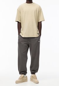 Beige bomulds T-shirt med rund hals, sammen med grå sweatpants med elastiske manchetter og beige sneakers med grå detaljer.