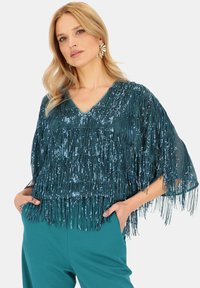 Miętowa bluzka z frędzlami i cekinami, dekoltem w serek i zwiewnymi rękawami; noszona z pasującymi miętowymi spodniami.