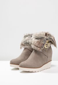 Grå ruskinds kileankle støvler med faux fur kant, guld lynlåsdetalje og struktureret hvid sål.
