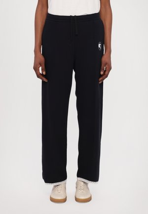 Navy sweatpants made of soft cotton, featuring a drawstring waist, side pockets, and a patterned trim at the hem, worn with light sneakers.