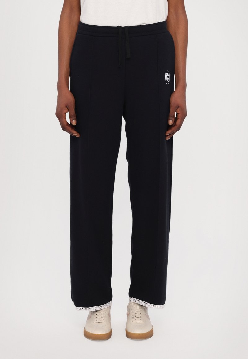 Navy sweatpants made of soft cotton, featuring a drawstring waist, side pockets, and a patterned trim at the hem, worn with light sneakers.