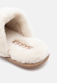 Μαλακή, κρεμ σε απόχρωση φλυστή παντόφλα με στρογγυλή μύτη και καφέ σόλα, με το λογότυπο της μάρκας "Socs" στο εσωτερικό.