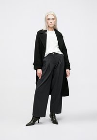 Svart ull trench coat, hvit bluse, grå vide bukser og svarte ankelstøvler. Jevne teksturer og skreddersydd design med strukturert silhuett.