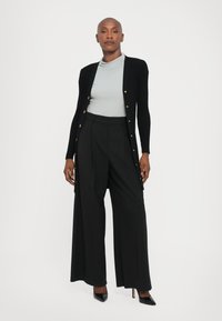 Black ribbed cardigan with gold buttons, light blue turtleneck, and wide-leg black trousers. Styled with black pointed heels.
