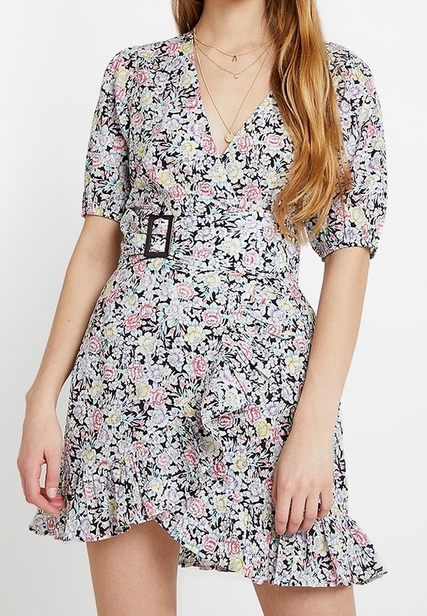 Vestido floral con mangas abullonadas, hebilla en la cintura, dobladillo con volantes y collares en capas en mujer con cabello largo.