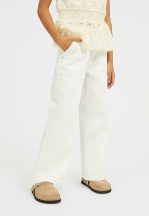Pantaloni in denim off-white a gamba larga, con tasche e orli arrotolati, abbinati a scarpe slip-on in suede beige. Tessuto leggero con una texture liscia.