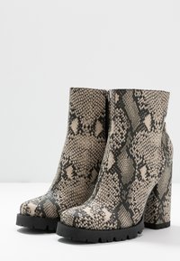 Bottines à motif peau de serpent en beige et noir ; doté d'un talon épais et d'une fermeture éclair latérale pour un enfilage facile. Détail de surface texturé.