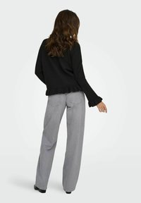 Pull en maille noir avec un ourlet et des poignets à volants, associé à un jean large taille haute gris clair. Texture lisse et coupe décontractée.