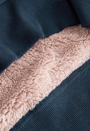 Tessuto foderato in pile con una texture costellata blu scuro sulla parte superiore e un morbido materiale rosa tenue sotto, che mostra un contrasto di colore e texture.