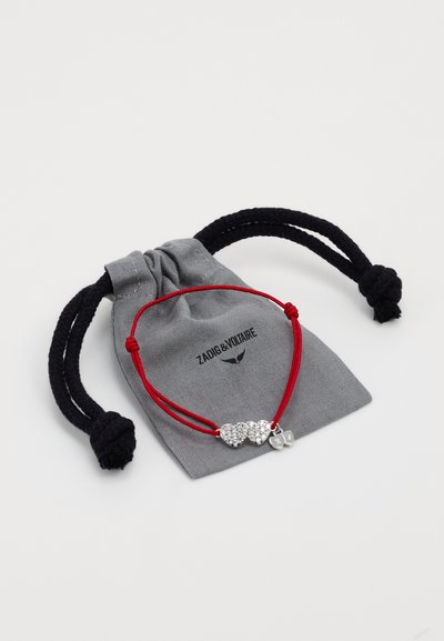 Red cord bracelet featuring three silver heart charms with attached clear rhinestones, displayed on a gray drawstring pouch.